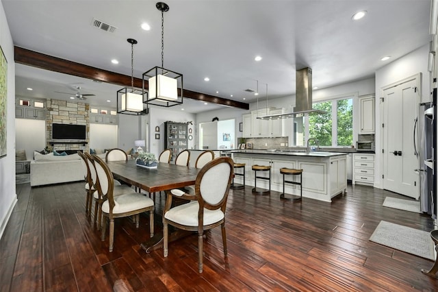 dining room featuring a barn door, ceiling fan, beamed ceiling, and dark wood-type flooring