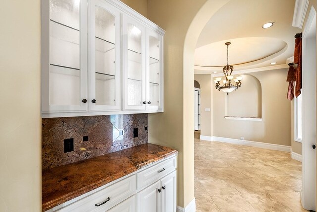 bar with dark stone counters, white cabinets, decorative backsplash, hanging light fixtures, and a chandelier