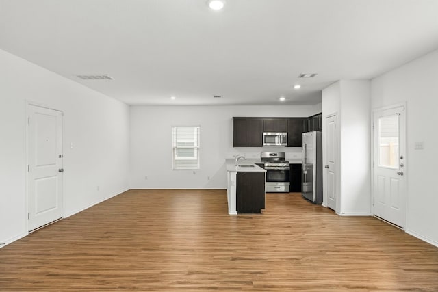 kitchen with dark brown cabinetry, sink, appliances with stainless steel finishes, a kitchen island with sink, and light hardwood / wood-style flooring