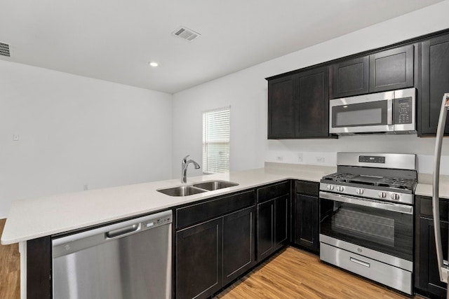 kitchen featuring kitchen peninsula, stainless steel appliances, sink, and light hardwood / wood-style flooring