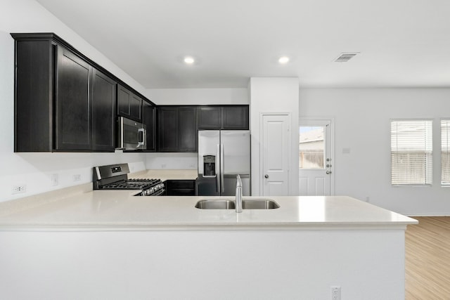 kitchen with kitchen peninsula, appliances with stainless steel finishes, sink, and light wood-type flooring