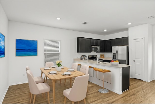 kitchen featuring light hardwood / wood-style floors, sink, kitchen peninsula, appliances with stainless steel finishes, and a kitchen bar