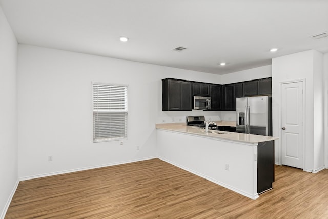 kitchen with kitchen peninsula, sink, light wood-type flooring, and appliances with stainless steel finishes