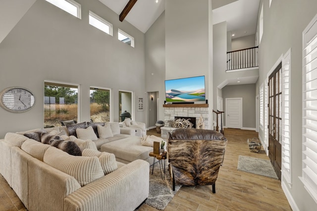 living room featuring high vaulted ceiling, beamed ceiling, a stone fireplace, and light hardwood / wood-style flooring