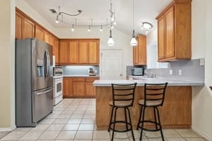 kitchen featuring light tile patterned flooring, kitchen peninsula, a breakfast bar area, decorative light fixtures, and stainless steel fridge