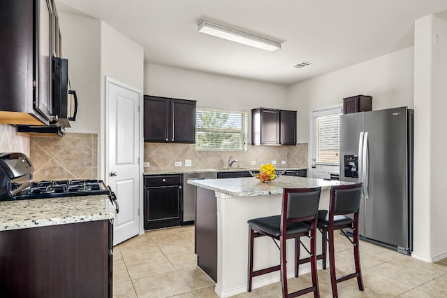 kitchen with tasteful backsplash, appliances with stainless steel finishes, dark brown cabinets, and a center island