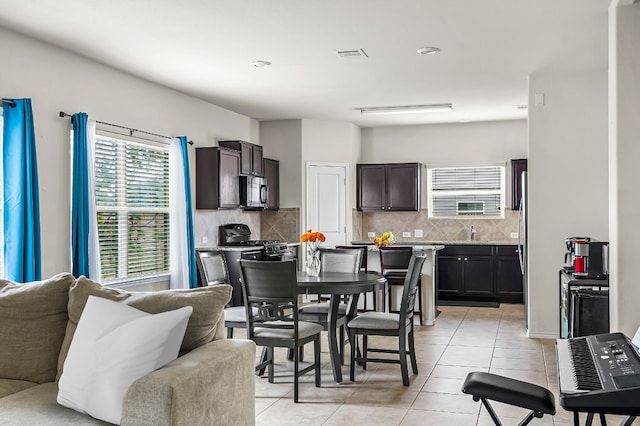 kitchen with stainless steel appliances, light stone counters, light tile patterned floors, backsplash, and dark brown cabinets