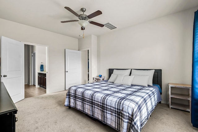 bedroom featuring light colored carpet, ceiling fan, and ensuite bath