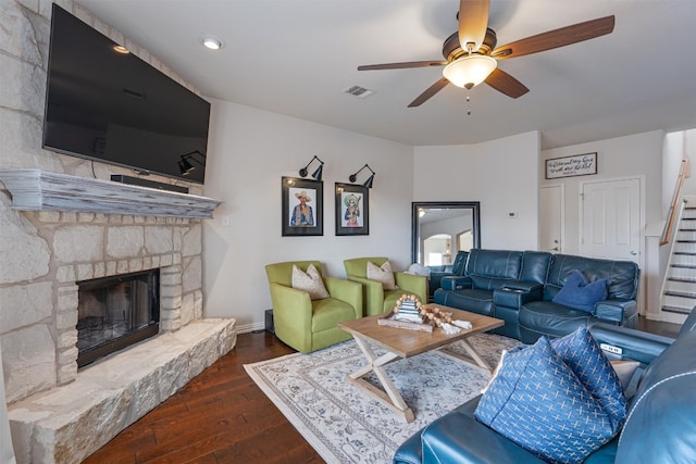 living room featuring a stone fireplace, ceiling fan, and dark hardwood / wood-style floors