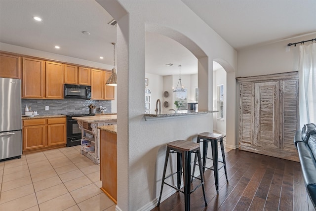 kitchen with light stone countertops, a kitchen bar, light wood-type flooring, black appliances, and pendant lighting