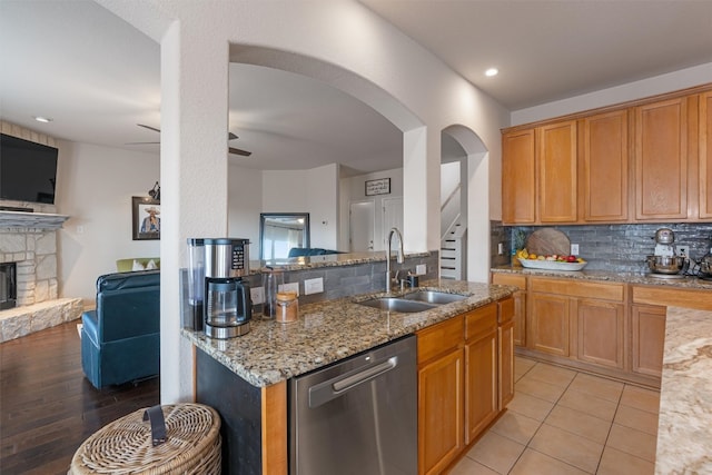 kitchen with a stone fireplace, sink, stainless steel dishwasher, decorative backsplash, and light wood-type flooring