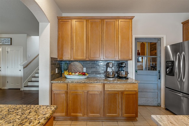 kitchen with stainless steel refrigerator with ice dispenser, light tile patterned floors, tasteful backsplash, and light stone counters