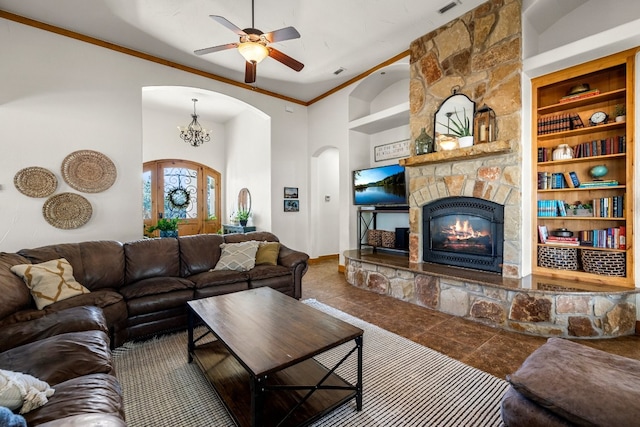 tiled living room featuring built in shelves, a stone fireplace, ceiling fan with notable chandelier, and crown molding