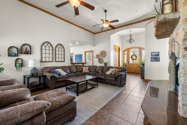 living room featuring high vaulted ceiling, a fireplace, ornamental molding, dark tile patterned flooring, and ceiling fan with notable chandelier