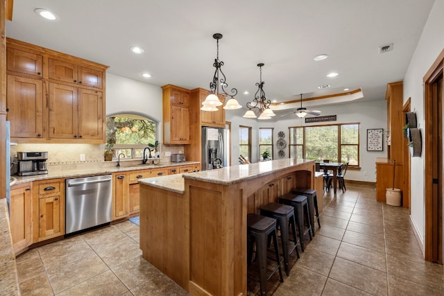 kitchen with tasteful backsplash, decorative light fixtures, a center island, appliances with stainless steel finishes, and a tray ceiling