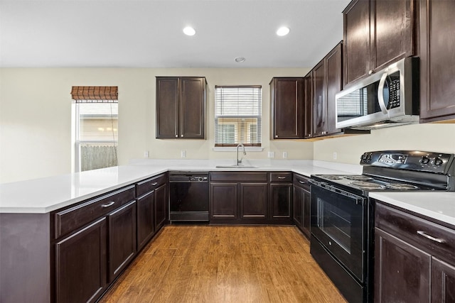 kitchen featuring dark brown cabinetry, sink, kitchen peninsula, hardwood / wood-style flooring, and black appliances