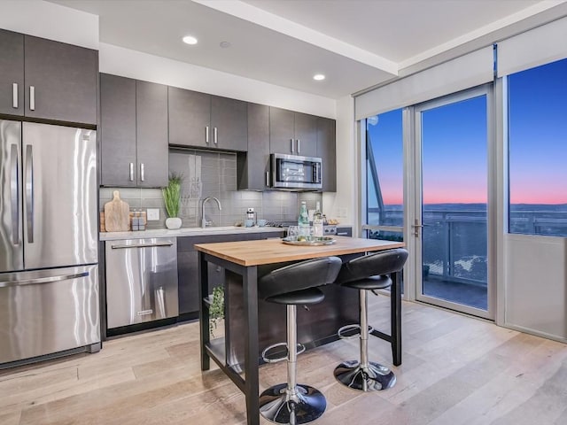 kitchen with wood counters, a breakfast bar, light wood-type flooring, appliances with stainless steel finishes, and decorative backsplash