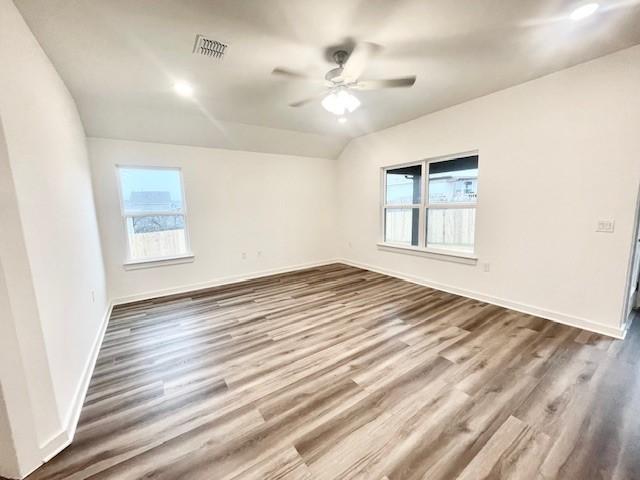 empty room with lofted ceiling, a wealth of natural light, wood-type flooring, and ceiling fan