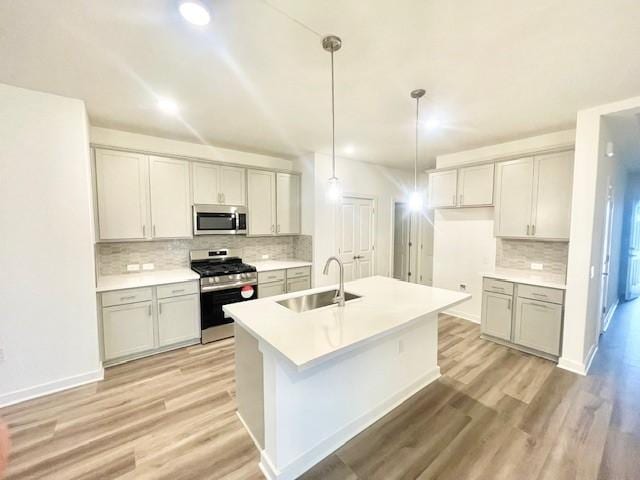 kitchen with sink, an island with sink, pendant lighting, stainless steel appliances, and light hardwood / wood-style floors