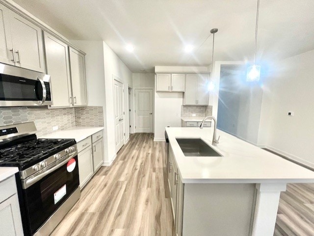 kitchen featuring appliances with stainless steel finishes, sink, decorative backsplash, hanging light fixtures, and a kitchen island with sink