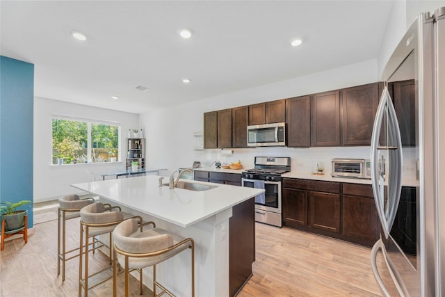 kitchen with light hardwood / wood-style floors, a center island with sink, sink, appliances with stainless steel finishes, and a breakfast bar area