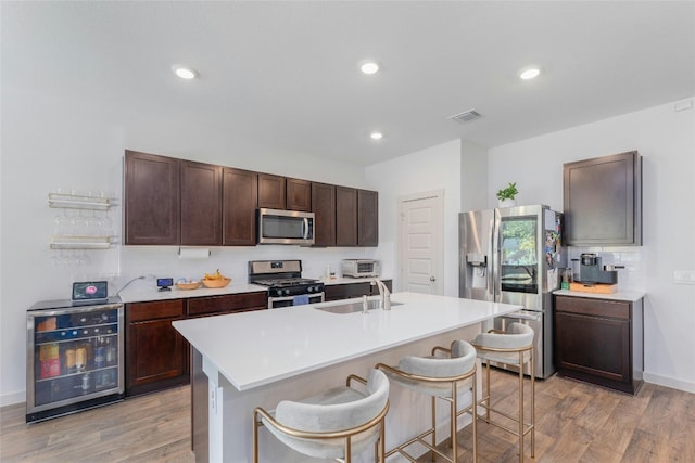 kitchen featuring appliances with stainless steel finishes, sink, an island with sink, a kitchen breakfast bar, and beverage cooler