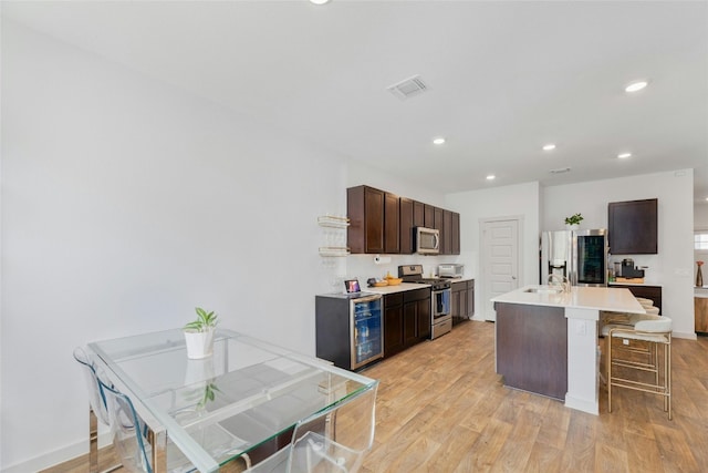 kitchen featuring light hardwood / wood-style floors, stainless steel appliances, a center island with sink, beverage cooler, and a breakfast bar