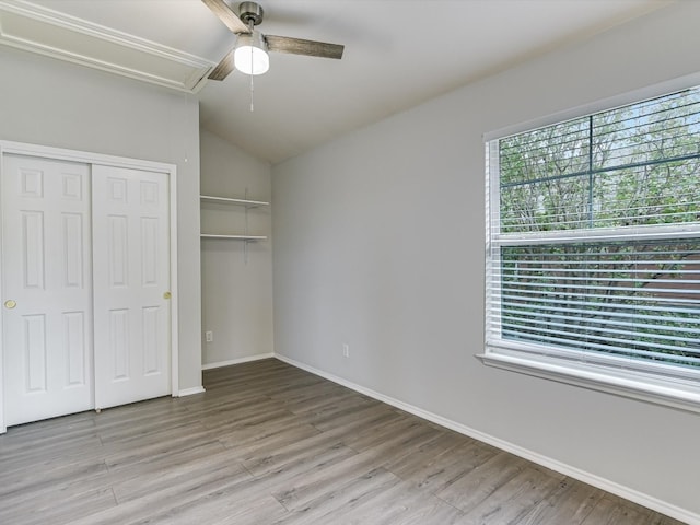 unfurnished bedroom featuring ceiling fan, multiple windows, light hardwood / wood-style flooring, and lofted ceiling