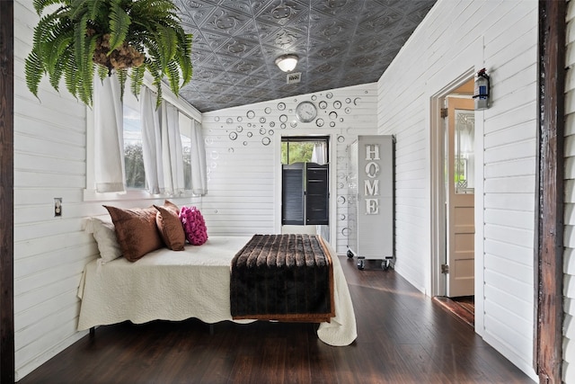 bedroom featuring lofted ceiling, wooden walls, and dark wood-type flooring