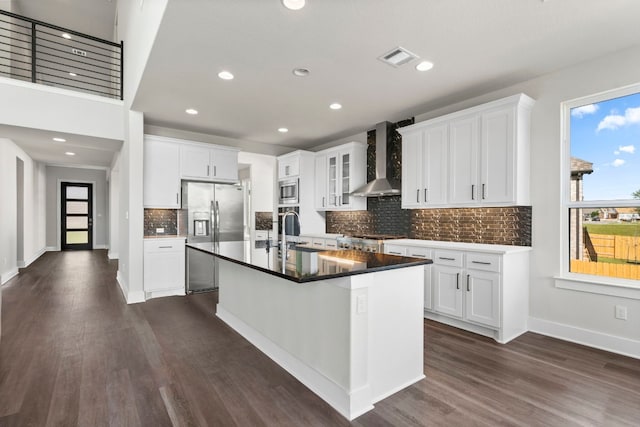 kitchen featuring stainless steel appliances, a center island with sink, white cabinetry, wall chimney exhaust hood, and dark hardwood / wood-style floors