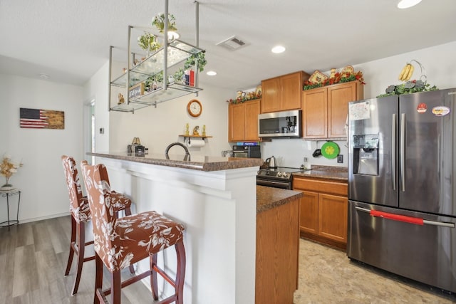 kitchen featuring appliances with stainless steel finishes, light hardwood / wood-style floors, a breakfast bar area, dark stone countertops, and a center island