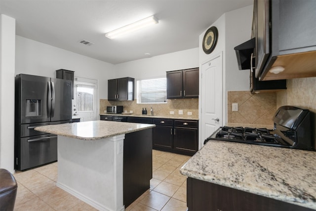 kitchen with light tile patterned flooring, decorative backsplash, a kitchen island, and stainless steel appliances