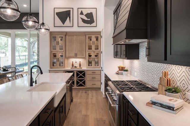 kitchen featuring hanging light fixtures, stainless steel stove, custom range hood, light hardwood / wood-style floors, and backsplash