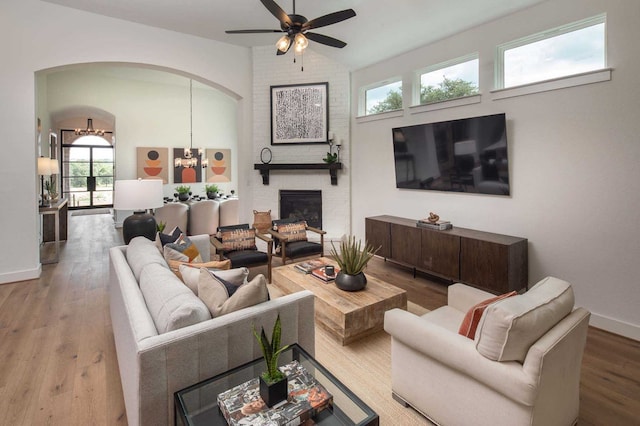 living room with arched walkways, lofted ceiling, a brick fireplace, wood finished floors, and baseboards