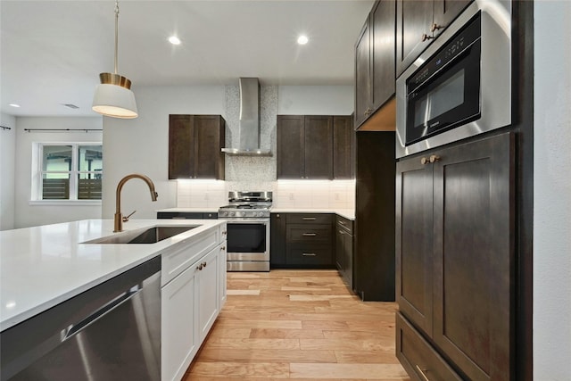 kitchen featuring light hardwood / wood-style floors, stainless steel appliances, sink, wall chimney range hood, and white cabinetry