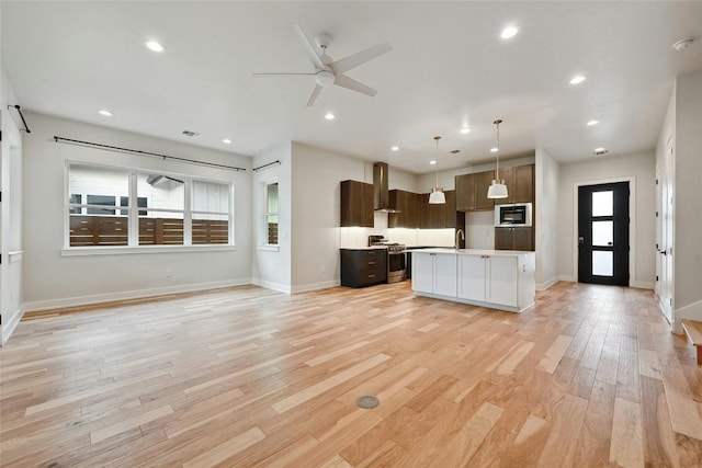 kitchen with appliances with stainless steel finishes, hanging light fixtures, a center island, wall chimney range hood, and light wood-type flooring