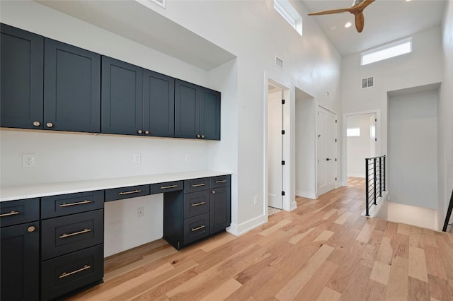 kitchen with a high ceiling, built in desk, ceiling fan, and light hardwood / wood-style flooring