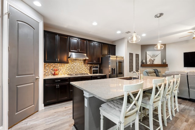 kitchen featuring a center island with sink, appliances with stainless steel finishes, a kitchen breakfast bar, decorative light fixtures, and light hardwood / wood-style flooring