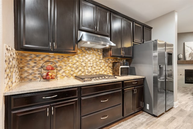 kitchen featuring dark brown cabinetry, light wood-type flooring, stainless steel appliances, and decorative backsplash