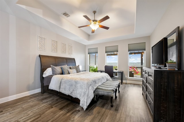 bedroom with dark hardwood / wood-style flooring, a tray ceiling, and ceiling fan