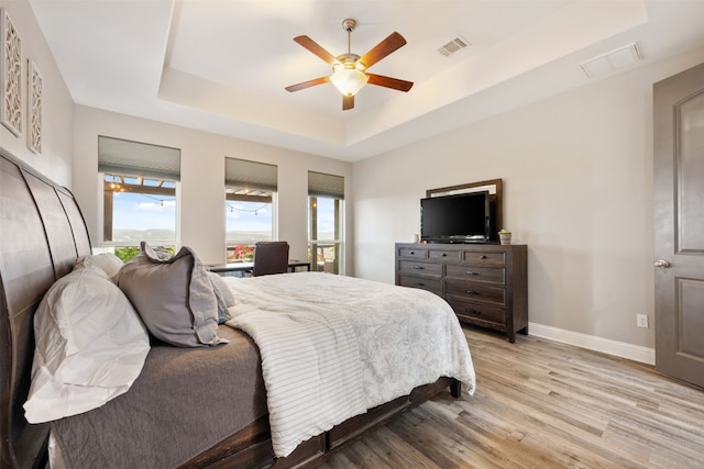 bedroom with light hardwood / wood-style floors, ceiling fan, and a raised ceiling