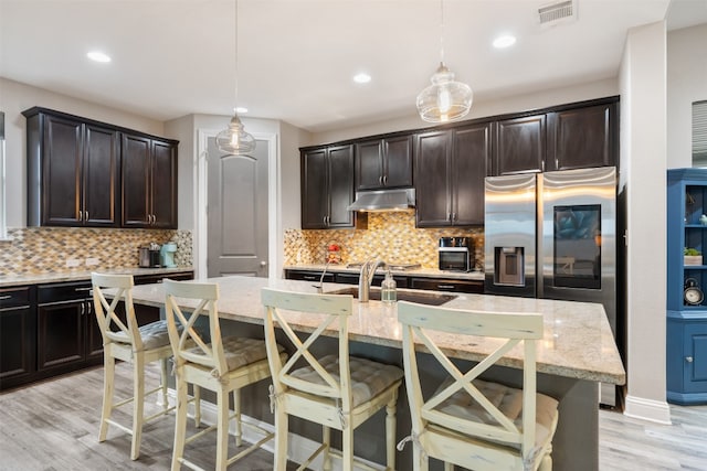 kitchen featuring a breakfast bar area, decorative backsplash, a kitchen island with sink, and decorative light fixtures