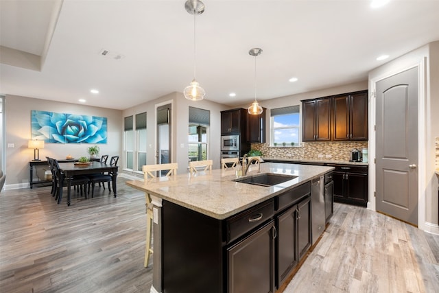 kitchen with an island with sink, a breakfast bar area, pendant lighting, and light wood-type flooring