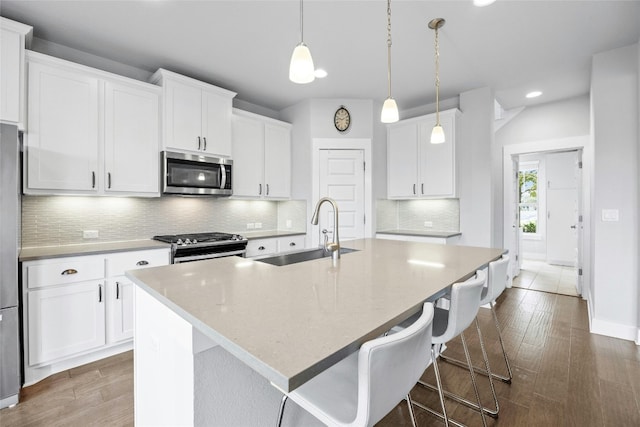 kitchen with stainless steel appliances, sink, hardwood / wood-style floors, a kitchen island with sink, and white cabinets