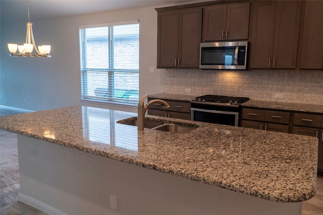 kitchen with light stone counters, backsplash, appliances with stainless steel finishes, dark brown cabinets, and sink