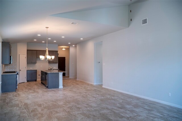 kitchen featuring a notable chandelier, hanging light fixtures, sink, a kitchen island with sink, and backsplash