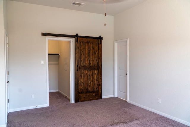 unfurnished bedroom with dark colored carpet, a barn door, a walk in closet, and a closet