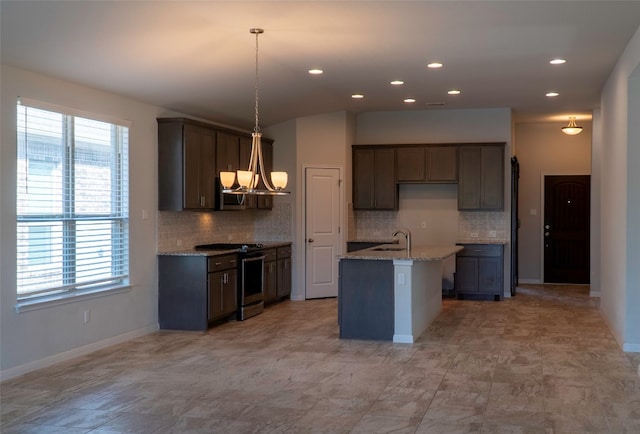 kitchen with pendant lighting, light stone countertops, stainless steel stove, and a kitchen island with sink