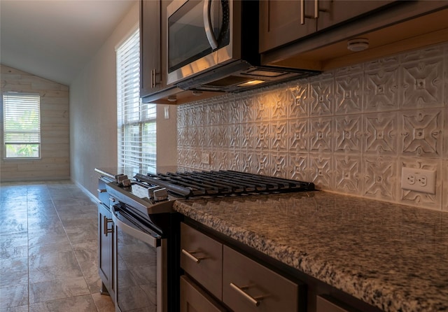 kitchen with appliances with stainless steel finishes, dark brown cabinets, decorative backsplash, dark stone countertops, and lofted ceiling