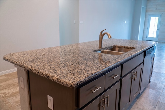 kitchen with a center island with sink, dark brown cabinetry, sink, stone counters, and stainless steel dishwasher